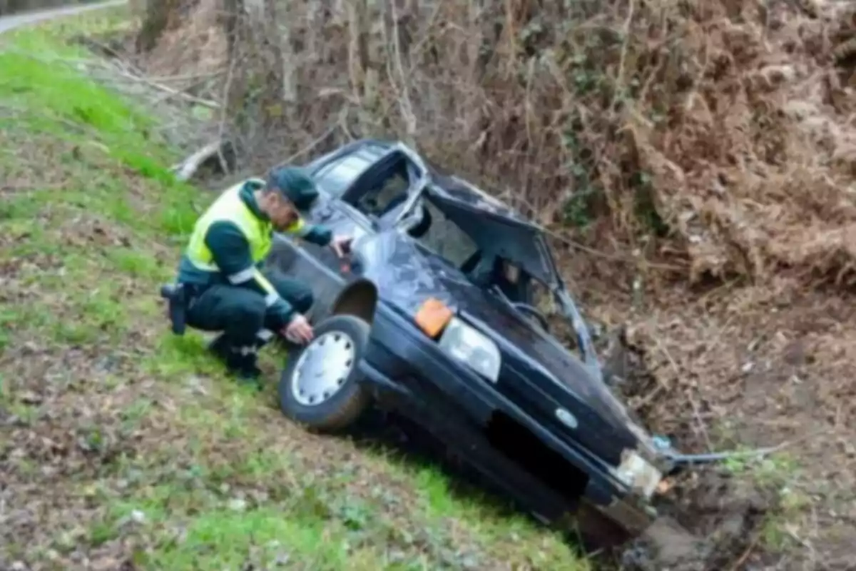 Un agente de tráfico inspecciona un coche accidentado en una zanja al lado de un camino rural.