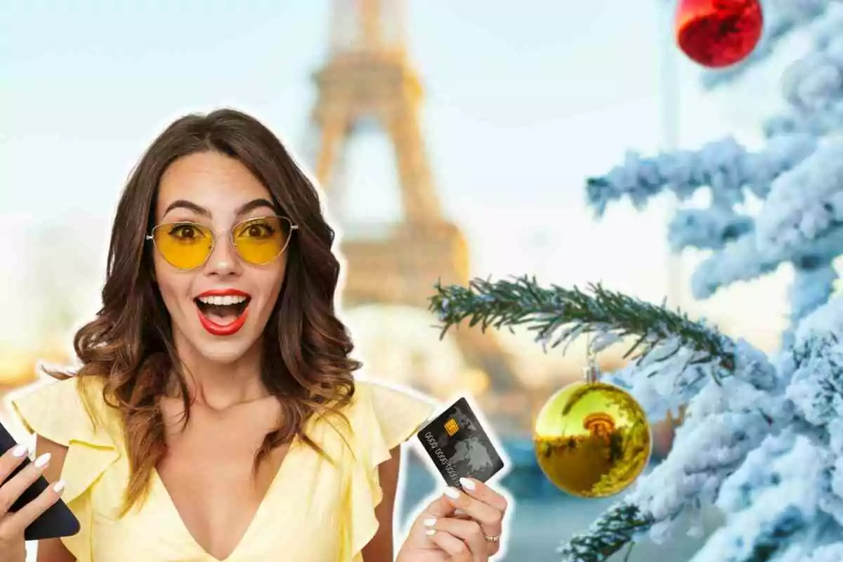 Mujer sonriente con gafas amarillas sosteniendo una tarjeta de crédito junto a un árbol de Navidad nevado con adornos y la Torre Eiffel de fondo.