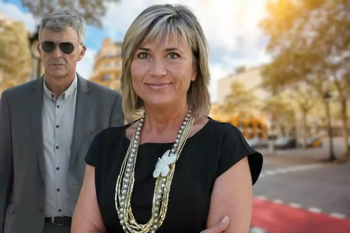 Una mujer sonriente con un collar de perlas y un hombre con gafas de sol en un entorno urbano.