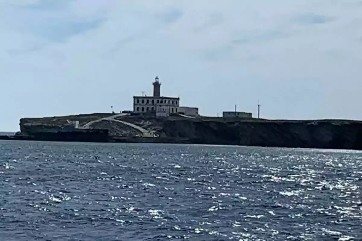 Un faro sobre un acantilado con el mar en primer plano y el cielo despejado.