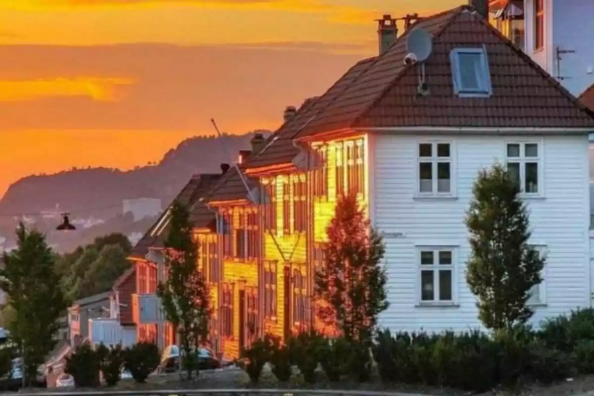 Casas blancas reflejando la luz del atardecer con un cielo naranja y montañas al fondo.